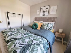 A bedroom with a bed, a wall-mounted drying rack, and a bedside table with a lamp.