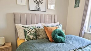 Una cama con una colcha de hojas verdes, varias almohadas y un cabecero.