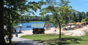 Relax by the serene lake with a boat docked nearby, a shaded pavilion, and comfortable beach chairs and umbrellas.