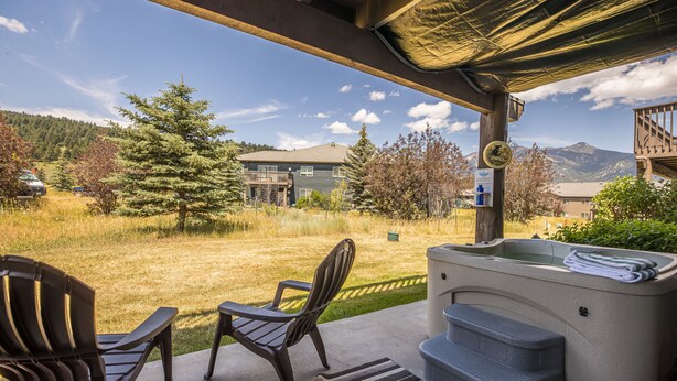 A covered patio with two Adirondack chairs, a hot tub, and a view of a mountain and residential buildings.