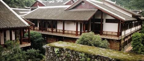A traditional Japanese building with multiple levels, wooden railings, and a stone wall in the foreground.