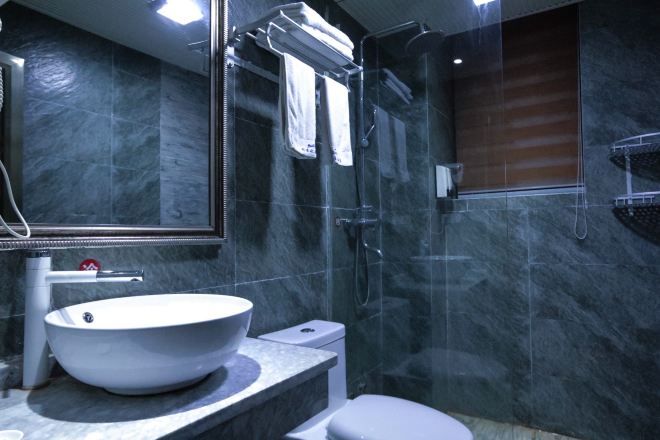 A modern bathroom with a large vessel sink, a glass-enclosed shower, and a marble-tiled wall.