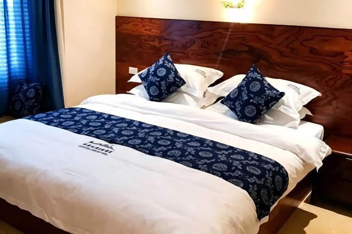 A hotel room with a wooden headboard, a bed with white and blue bedding, and a patterned throw.