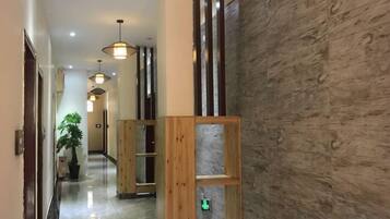 Corredor de hotel com divisórias de madeira, uma planta em vaso e luminárias pendentes.