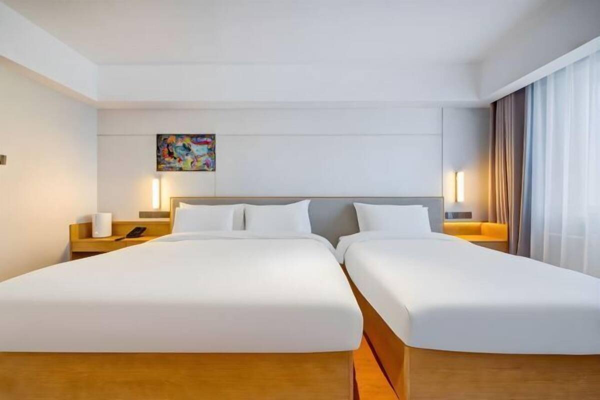 A hotel room with two beds, a painting on the wall, and a nightstand with a lamp.