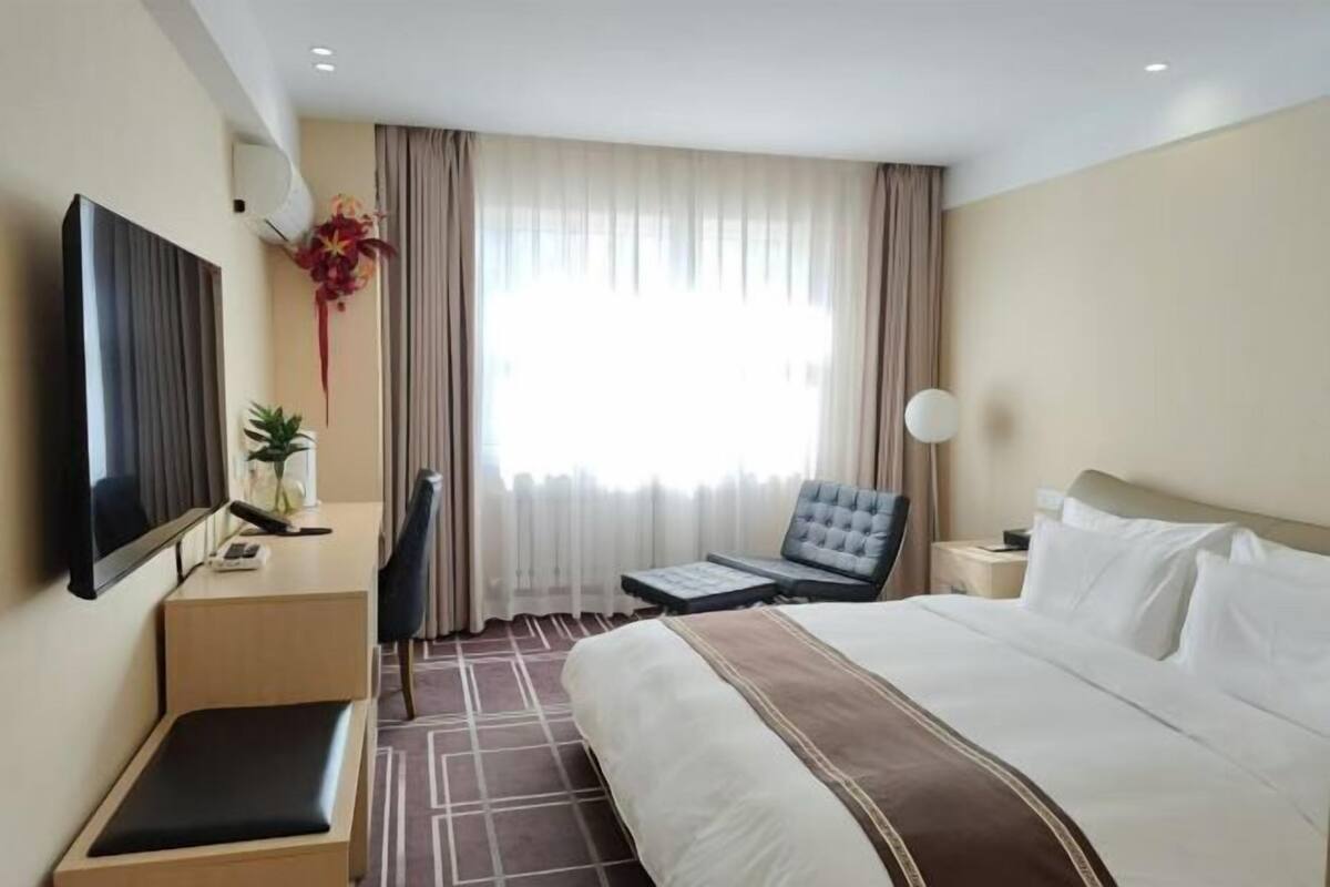 A hotel room with a bed, a desk with a chair, a television, and a window with curtains.