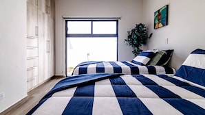 Ein Schlafzimmer mit zwei Betten, einer Schiebetür zu einem Balkon, einem Blumentopf und einem Bild an der Wand.