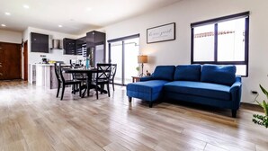 Ein modernes Wohnzimmer mit einem blauen Sofa, einem Essbereich mit Tisch und Stühlen sowie einer Küche im Hintergrund.