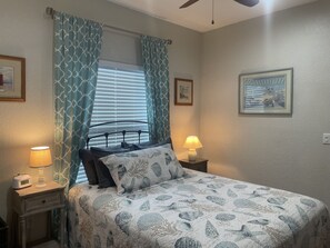 A bedroom with a bed, two bedside lamps, a window with curtains, and framed pictures on the walls. - Only 2 blocks from all the action on Canal Street! (New Smyrna Beach)