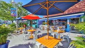 Een terras met tafels en stoelen, een grote parasol en een gebouw met een blauw luifel.