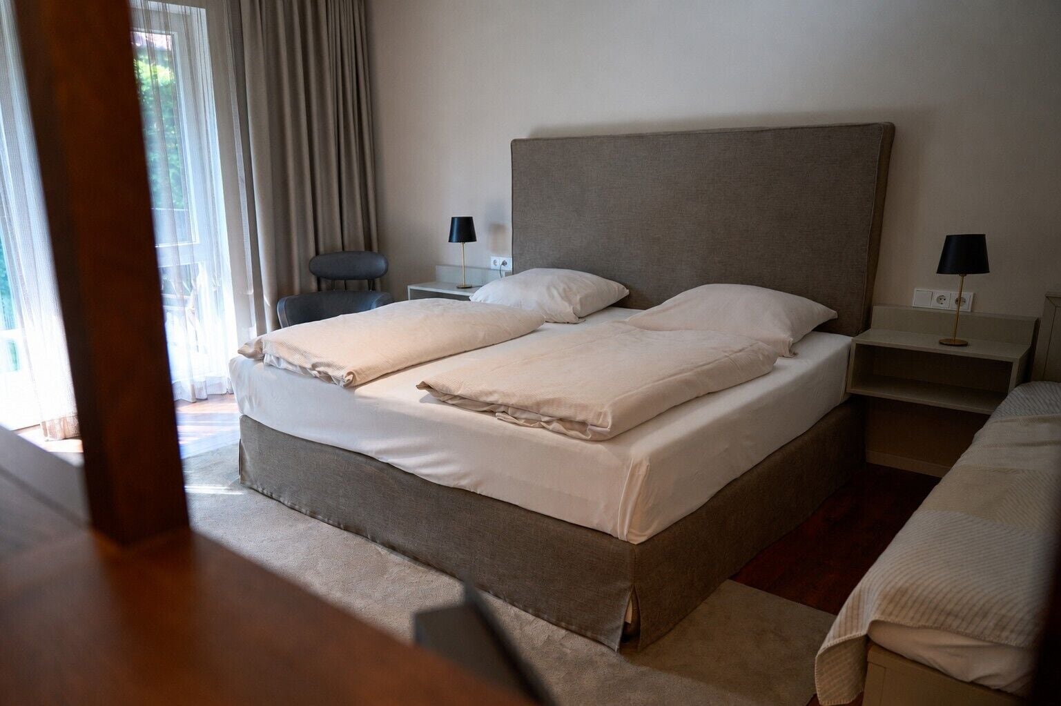 A neatly made double bed with a headboard, two bedside tables with lamps, and a chair.