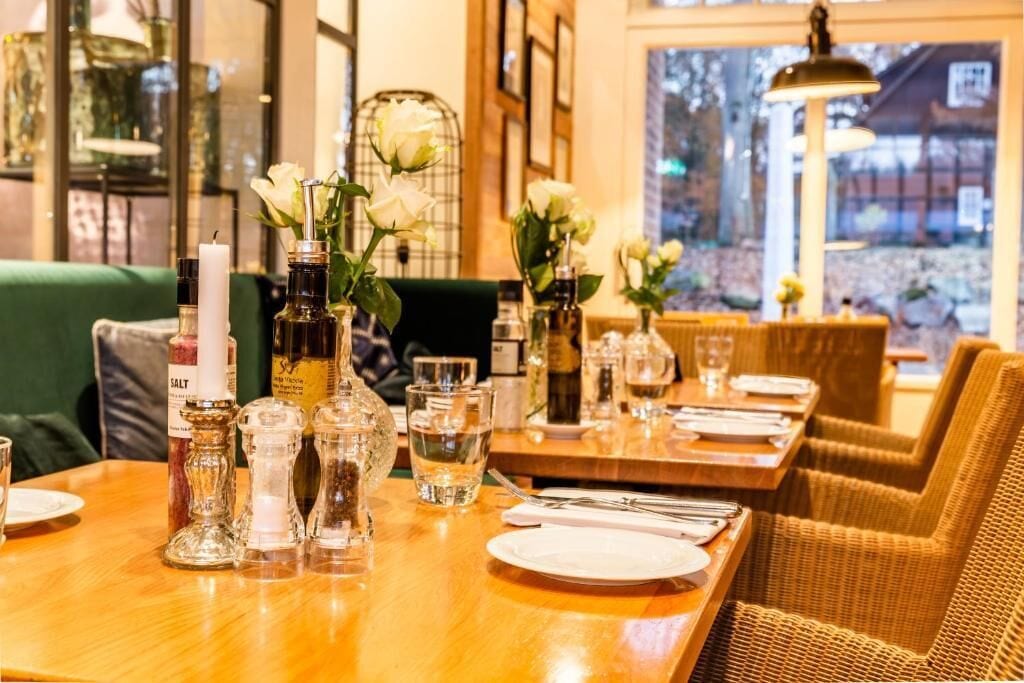 Een restaurant met houten tafels, gedekt voor een maaltijd, zout- en pepervaatjes en witte bloemen.