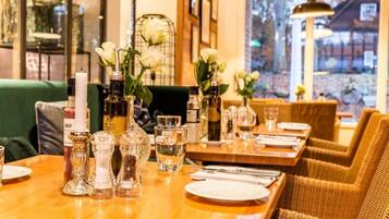 Een restaurant met houten tafels, gedekt voor een maaltijd, zout- en pepervaatjes en witte bloemen.