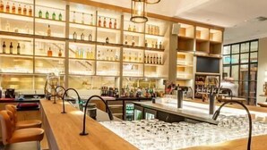 A spacious bar area with a long counter, multiple seating options, and a variety of bottles on shelves. - Hotel Gut Altona (Dötlingen)
