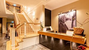 A hotel reception area with a wooden staircase, a reception desk, and a large framed photograph on the wall. - Hotel Gut Altona (Dötlingen)
