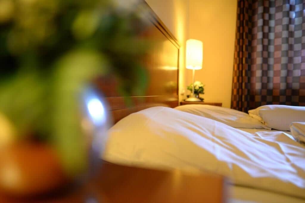 Une chambre d’hôtel avec un lit, une table de chevet, une lampe et un rideau à carreaux.