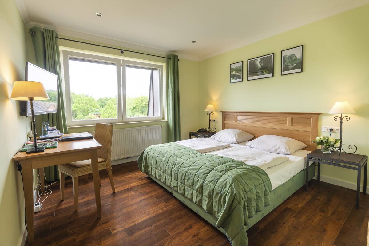 Ein Schlafzimmer mit einem Bett, einem Schreibtisch, einem Stuhl, zwei Nachttischen mit Lampen, einem Heizkörper und zwei gerahmten Bildern an der Wand.