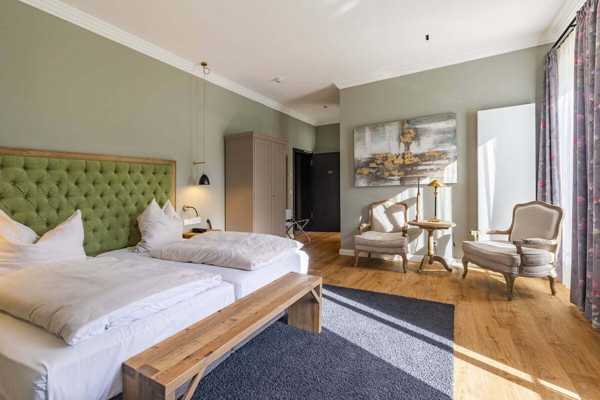 Ein Hotelzimmer mit einem großen Bett, einer Bank, zwei Stühlen, einem kleinen Tisch und einem Kleiderschrank.