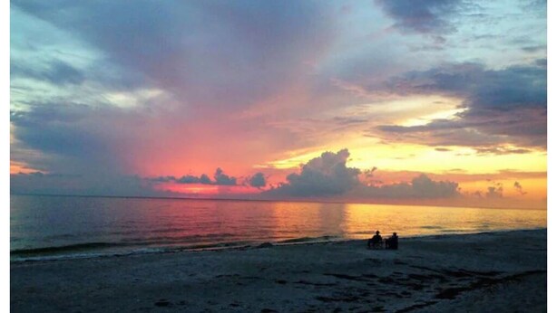 A beach at sunset with a calm sea and a few people in the distance. - Serenity Canal Cottage 2/2 on Gulf Access Canal!! (North Port)