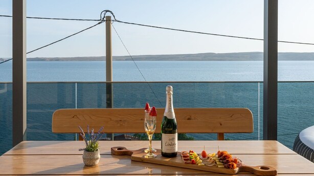A table with a bottle of Lindermor champagne, a glass of white wine, and a wooden board with snacks. - Rina Apartments - Superior One Bedroom Apartment with Terrace and Sea View (Baric Draga)