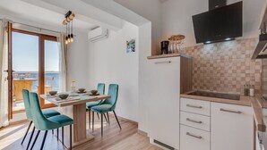 A modern kitchen with white cabinets, a black TV, and a wooden dining table with teal chairs. - Rina Apartments - Superior One Bedroom Apartment with Terrace and Sea View (Baric Draga)