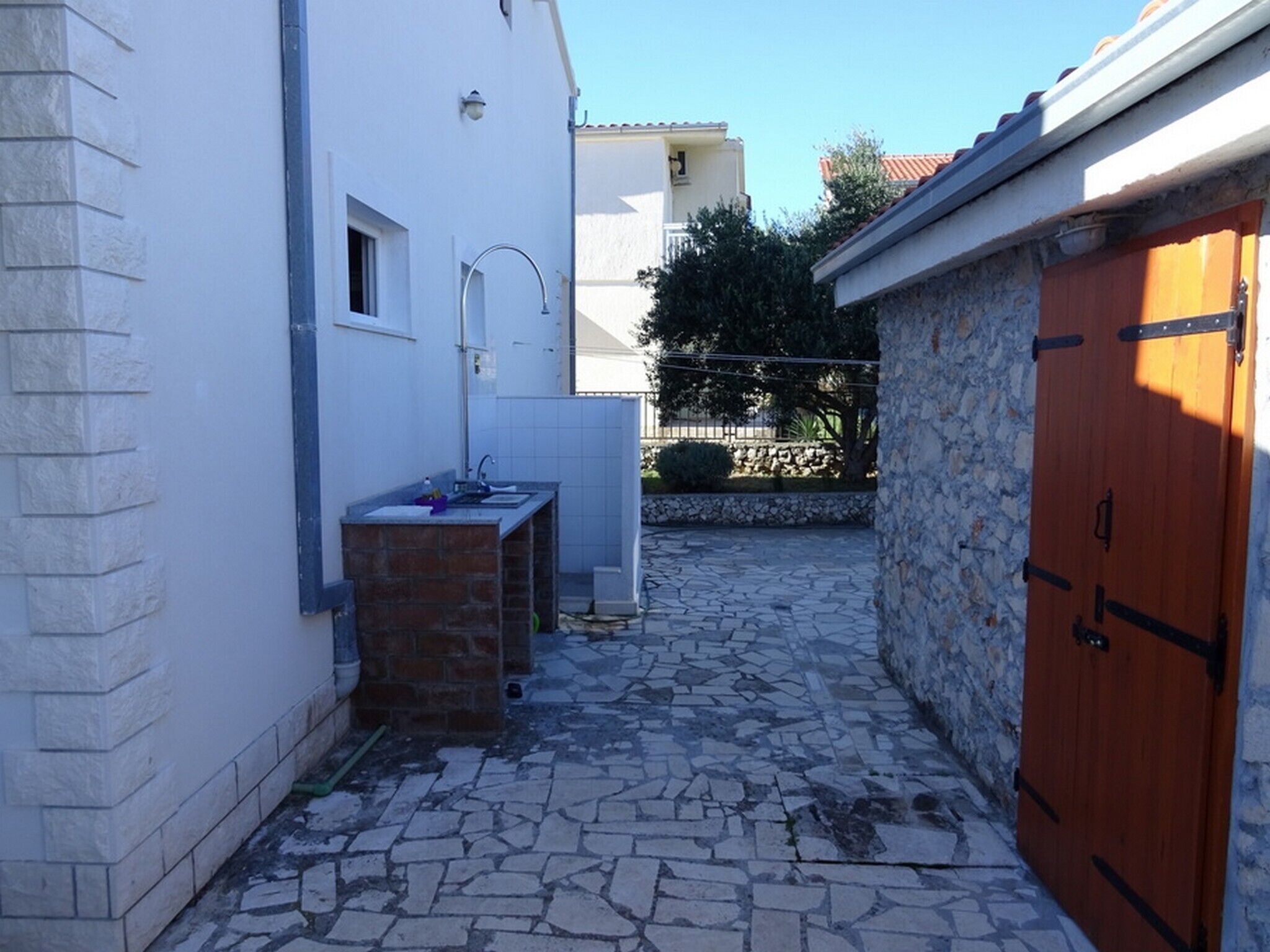 A narrow courtyard with a stone floor, a small sink, and a wooden door.
