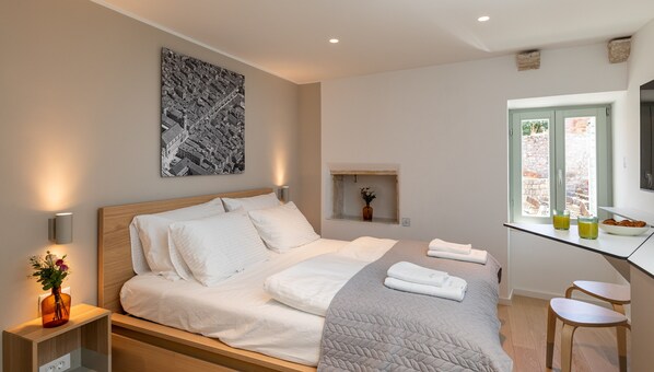 Ein modernes Schlafzimmer mit einem großen Bett, einem Nachttisch mit Lampe, einem kleinen Fenster mit Ausblick und einem Wandbild.