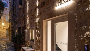 Edifici de pedra amb un rètol que diu "UNIKSE" i una porta amb un panell de vidre. Hi ha taules i cadires a l'exterior, i una planta en test.