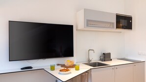 Una cocina moderna con una televisión de pantalla plana, un microondas, un lavabo y una encimera con un bol de comida y vasos de zumo.