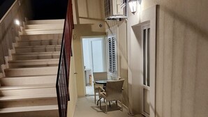 Un escalier menant à un espace repas comprenant une table et des chaises, un climatiseur fixé au mur et une porte avec une fenêtre.