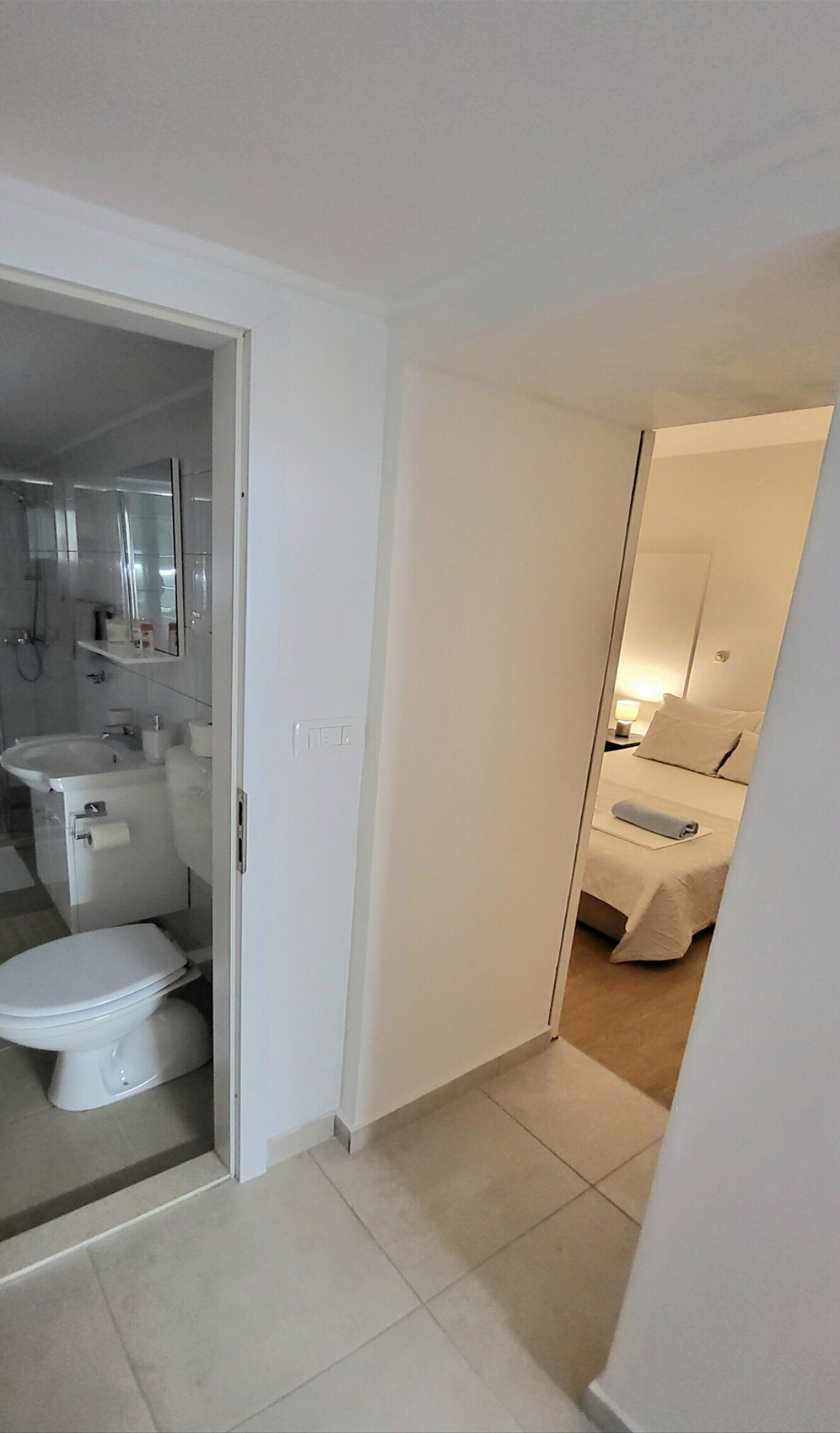 Habitación de hotel con baño que incluye inodoro, lavamanos y espejo. La habitación tiene una cama con almohada y manta.