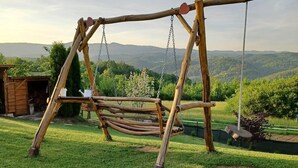 Un ensemble de balançoires en bois installé dans une cour verdoyante, avec vue sur des collines lointaines.