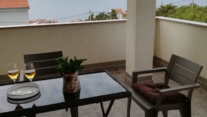 Ein Balkon mit Tisch, zwei Stühlen, einem Blumentopf und zwei Weingläsern.