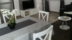 Ein modernes Wohnzimmer mit Essbereich, einem Flachbildfernseher, einem weißen Schrank und einem kleinen runden Tisch mit einer Pflanze.
