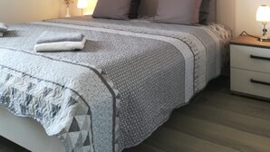 Ein ordentlich bezogenes Bett mit gemustertem Überwurf und Kissen, ein Nachttisch mit Lampe sowie ein Wandbild über dem Bett.