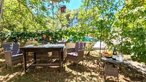 An outdoor patio with wicker furniture, a table set with a bottle and fruit bowl, and a birdhouse hanging above.