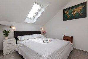 A bedroom with a skylight, a world map on the wall, a bed with white bedding, a nightstand with a plant, and a wooden chair.