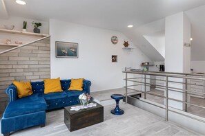 A modern living room with a blue sofa, wooden shelves, a staircase, and a kitchen area.