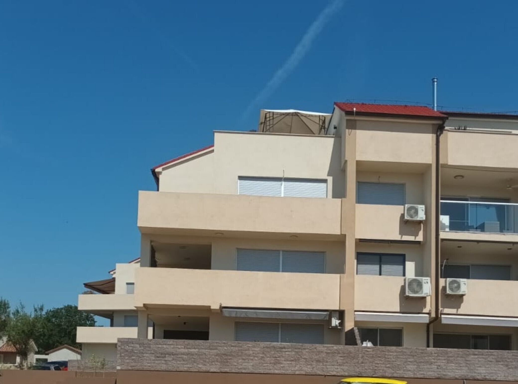 Un immeuble à plusieurs étages doté de balcons, de climatiseurs et d’un toit rouge.