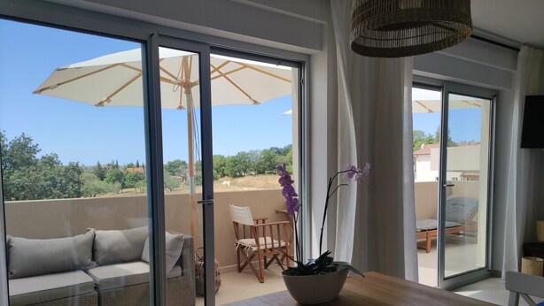 Un balcón con sofá, mesa de comedor y sillas, y vistas a zonas verdes y edificios.