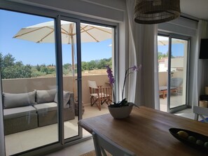 Un balcón con sofá, mesa de comedor y sillas, y vistas a zonas verdes y edificios.