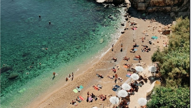 Una playa con agua cristalina, acantilados rocosos y gente tomando el sol.
