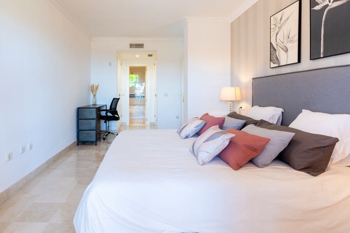 Une chambre d’hôtel avec un grand lit, un bureau avec une chaise et une vue sur un couloir.