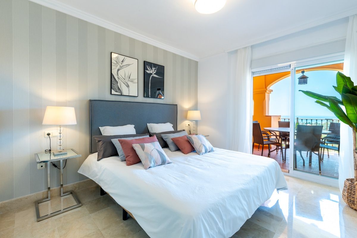A hotel room with a large bed, two bedside tables, and a balcony with outdoor seating.