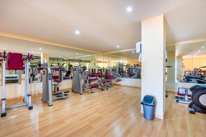 Une salle de sport équipée de divers appareils d’exercice, dotée d’un plancher en bois et d’une poubelle.