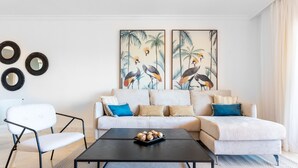 A modern living room with a white sofa, black coffee table, and a chair. There are three framed artworks on the wall and a small tray of snacks on the coffee table. - Resort Mediterra II | Apartment with Sea View (Benalmádena)