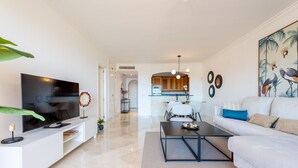 A modern living room with a flat-screen TV, a sofa, a coffee table, and a dining area in the background. - Resort Mediterra II | Apartment with Sea View (Benalmádena)