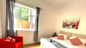 Una camera da letto con un letto, una poltrona rossa, una finestra con tende e un quadro appeso al muro.