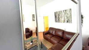 Un soggiorno moderno con un divano in pelle marrone, un divisorio in vetro e un grande quadro astratto appeso alla parete.