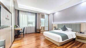 A hotel room with a wooden floor, a bed with a grey headboard, a desk with a chair, and a large window with curtains. - Bohai Hotel （Taishan Chonglou) (Taishan)